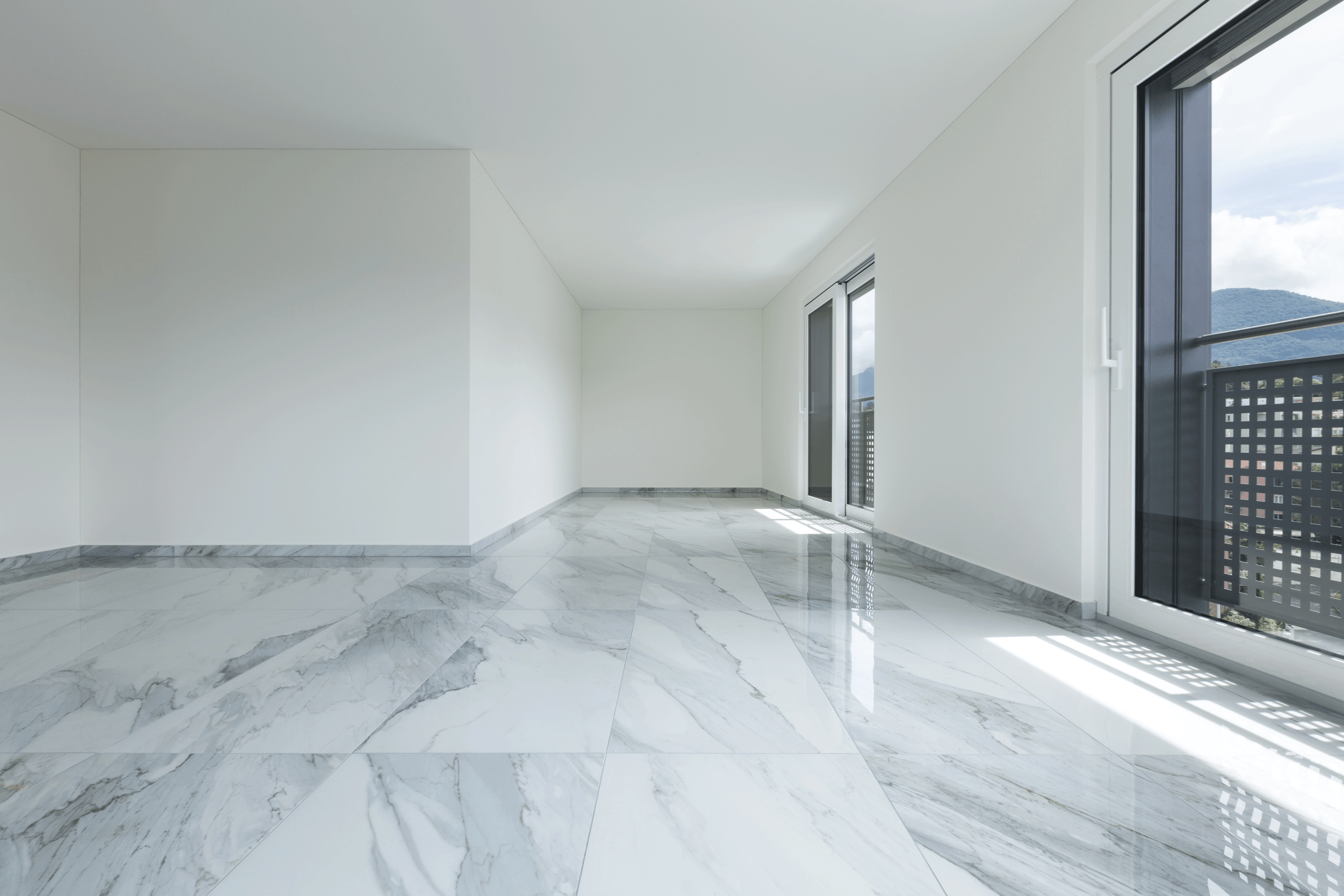 Innenansicht eines leeren Appartments mit weißen Wänden, deckenhohen Fenstern und weißem Marmorboden