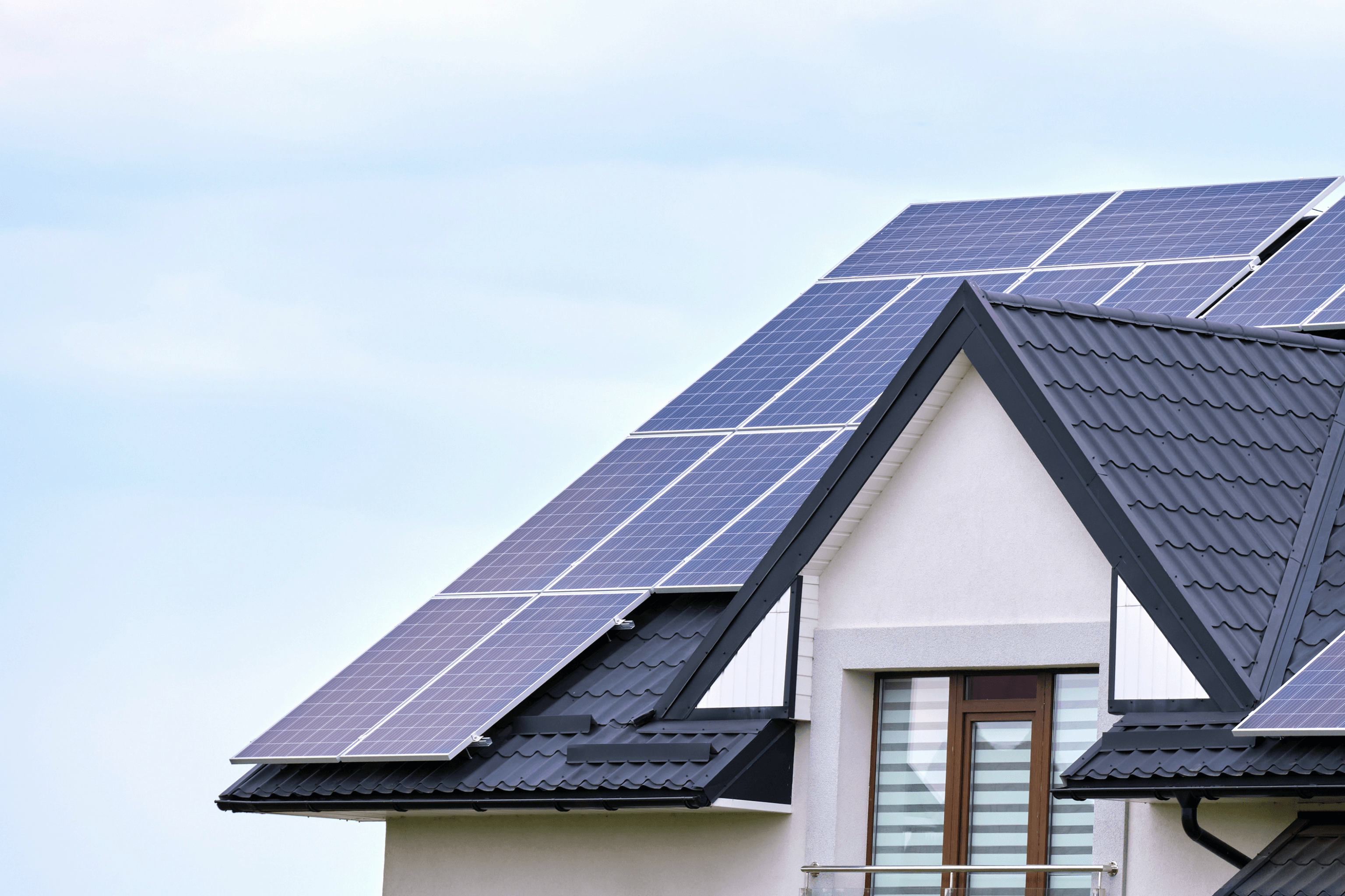 Weißes Haus mit blauen Dachkacheln und einer darauf montierten Solaranlage an einem sonnigen Tag